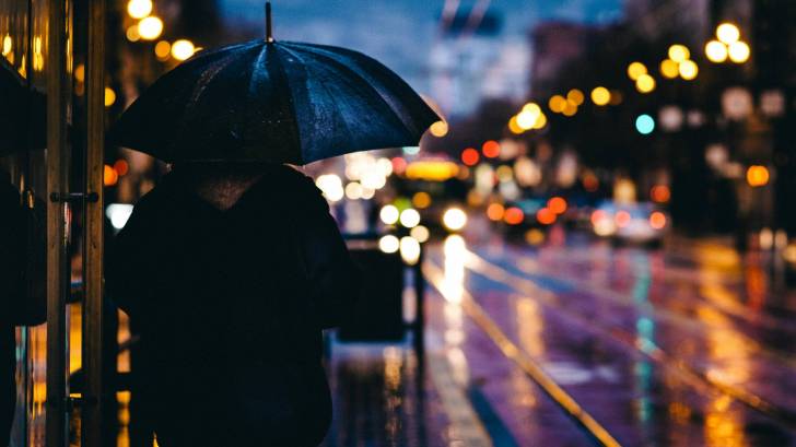 adult with an umbrellaon a rainy street with lights on it