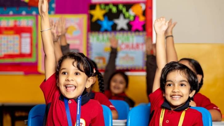 young children in school happy and raising hands