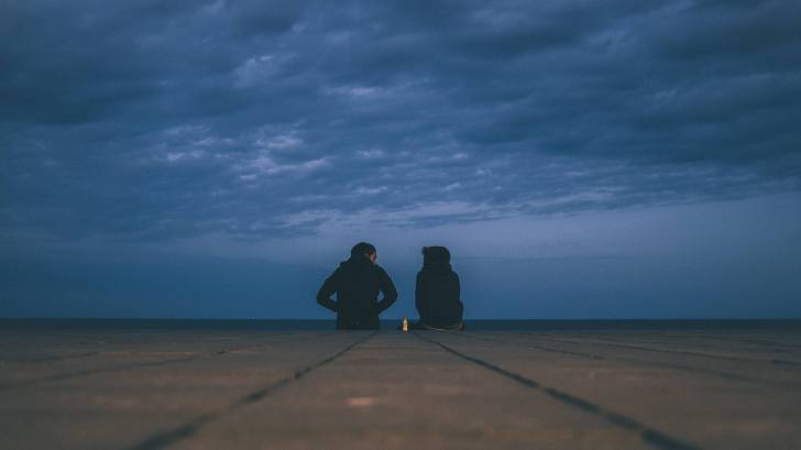 young couple sitting on the end of a dock talking at night