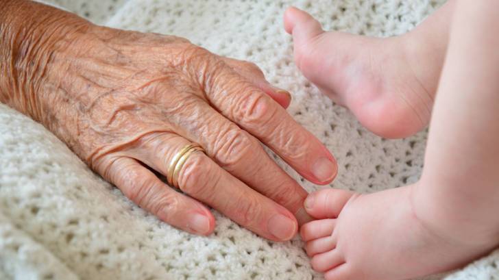 grandma's hand in crib with baby feet, generations