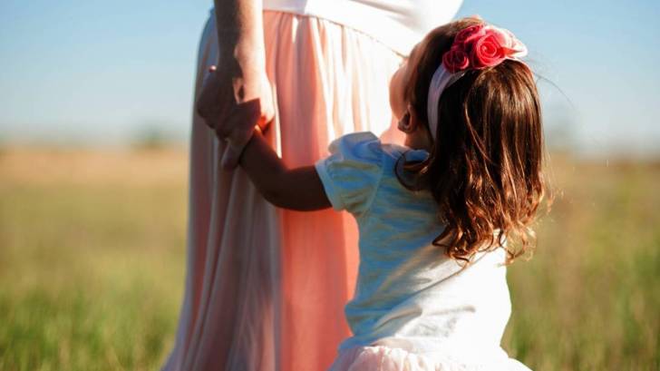 pregnant mom and daughter standing in a field