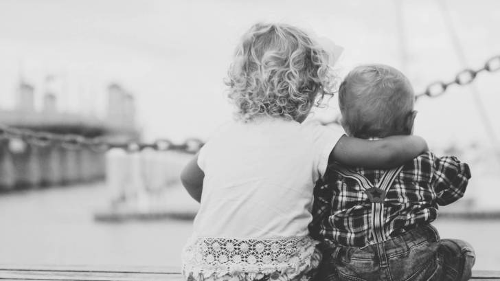 siblings hugging each other sitting on a dock