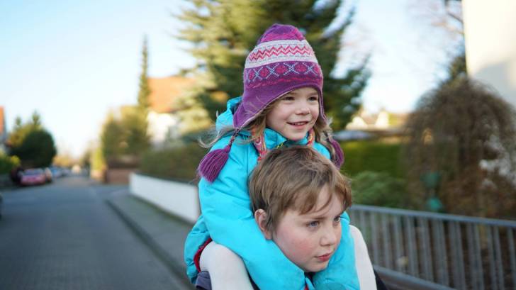 little sister riding on her borthers shoulders happy dressed warm