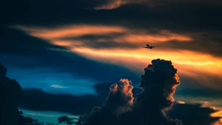 plane flying in the sky, with cloouds and sun setting