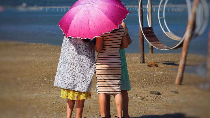 women on a beach protecting from the sun with an umbrella