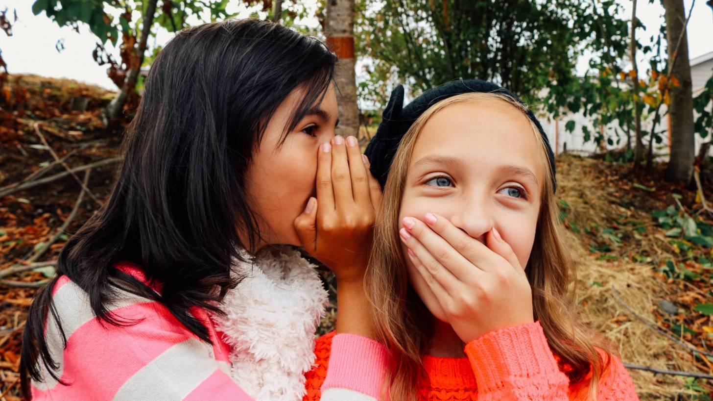 2 young girls telling secrets and whispering