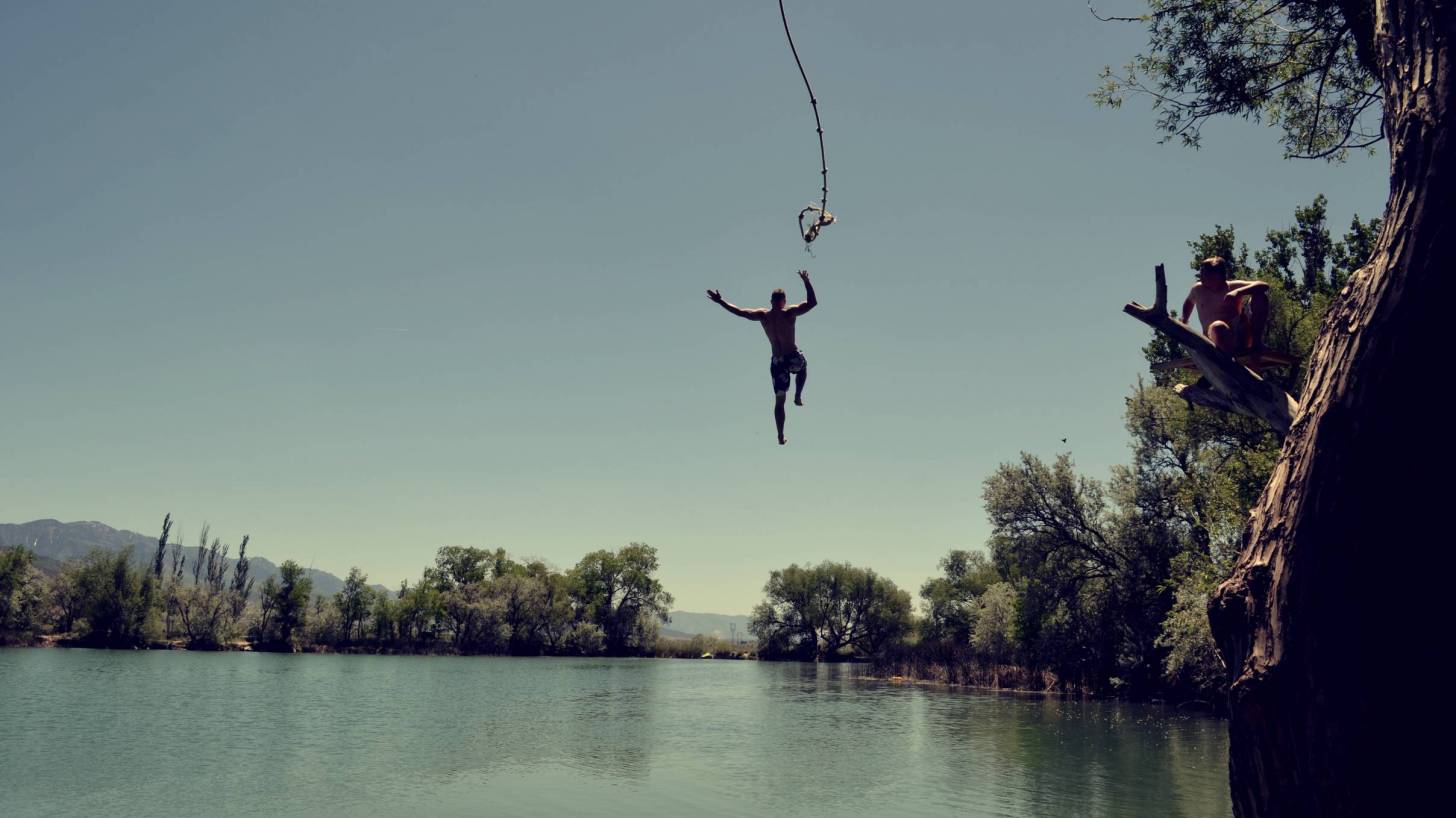 man swinging from a rope over a lake and letting go