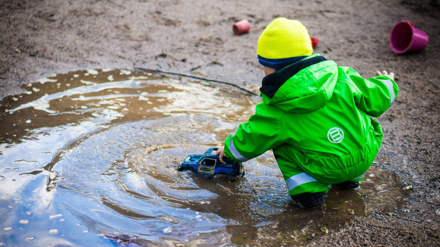 healthy child playing with a truck in a puddle