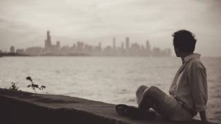 man sitting on a sea wall looking back at the city