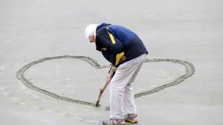 older man drawing a heart on beach